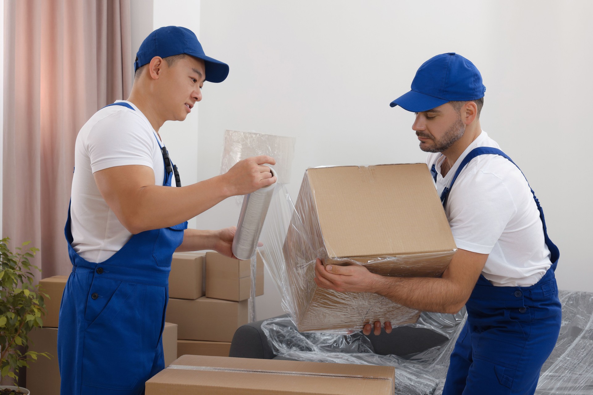 Workers wrapping box in stretch film indoors